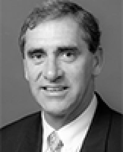 Black and white head shot of John Fahey, former Minister for Finance and Administration. He is smiling and wearing a dark jacket, white shirt and tie.