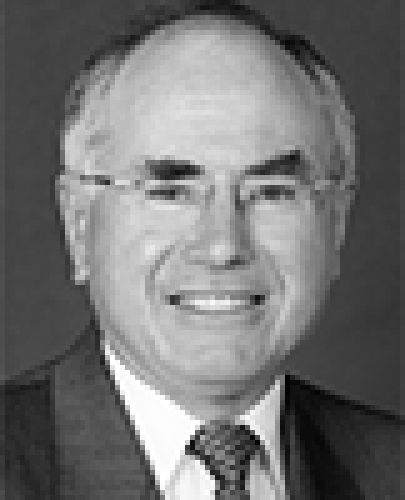 Black and white head shot of John Howard, former Minister for Finance. He is smiling and is wearing a dark jacket, shirt, and tie. 