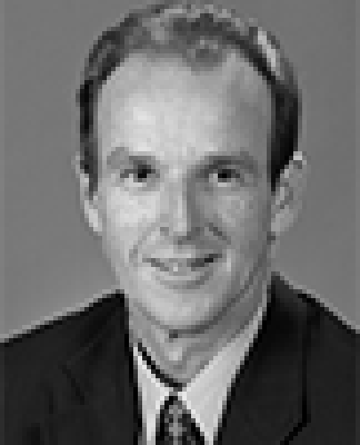 Black and white head shot of Joe Ludwig, former Special Minister of State. He is smiling and wearing a dark suit jacket, shirt, and tie.