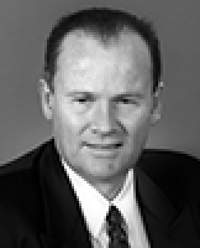 Black and white head shot of Lindsay Tanner, former Minister for Finance and Deregulation. He is smiling and wearing a dark jacket, white shirt and tie.