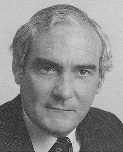 A black and white head shot of Eric Robinson, who is wearing a dark jacket, shirt and tie. 