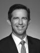 Black and white head shot of Simon Birmingham, former Minister for Finance. He is smiling and wearing a suit, shirt and tie.