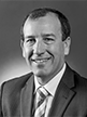 Black and white head shot of Mal Brough, former Special Minister of State. He is smiling, wearing a dark suit, shirt and tie.