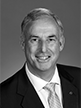 Black and white head shot of Richard Colbeck, former Parliamentary Secretary to the Minister for Finance and Administration. He is smiling and wearing a dark suit jacket, white shirt and a tie. 