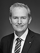 Black and white head shot of David Coleman, former Assistant Minister for Finance. He is smiling, wearing a dark suit jacket, white shirt and striped tie. 