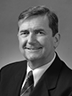 Black and white head shot of Chris Ellison, former Special Minister of State. He is smiling broadly and is wearing a dark suit jacket, white shirt and a tie. 