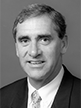 Black and white head shot of John Fahey, former Minister for Finance. He is smiling and wearing a dark jacket, white shirt and tie.