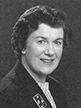 Black and white head shot of Dame Margaret Guilfoyle, former Minister for Finance. She is smiling and wearing a dark blazer, with a brooch on her lapel.