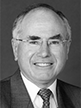 Black and white head shot of John Howard, former Minister for Finance. He is smiling and is wearing a dark jacket, shirt, and tie. 