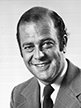 Black and white head shot of Sir Phillip Lynch, former Special Minister of State. He is smiling, wearing a light coloured jacket, white shirt and tie. 