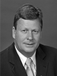 Black and white head shot of Michael Ronaldson, former Special Minister of State. He is wearing a dark suit jacket, white shirt and tie.