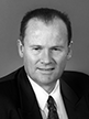 Black and white head shot of Lindsay Tanner, former Minister for Finance and Deregulation. He is smiling and wearing a dark jacket, white shirt and tie.