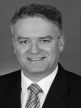 A black and white head shot of Mathias Cormann, who is smiling and wearing a dark jacket, shirt and tie. 