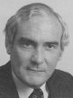 A black and white head shot of Eric Robinson, who is wearing a dark jacket, shirt and tie. 