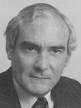 A black and white head shot of Eric Robinson, who is wearing a dark jacket, shirt and tie.