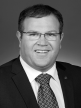 A black and white head shot of Ben Morton, who is smiling and wearing a dark suit, shirt and tie. 